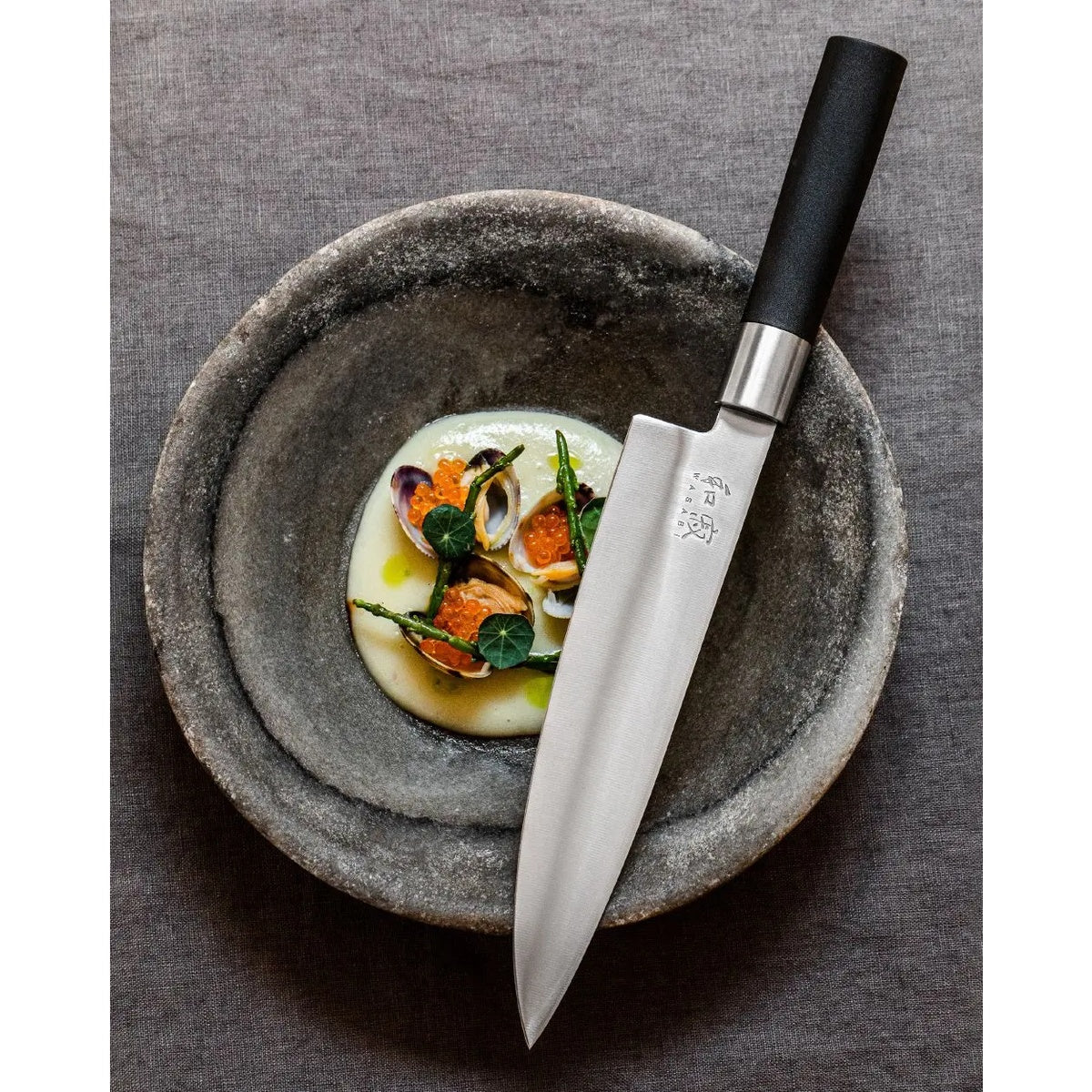 KAI Wasabi Black – Original-Serienfoto mit Kochmesser auf einem Teller.