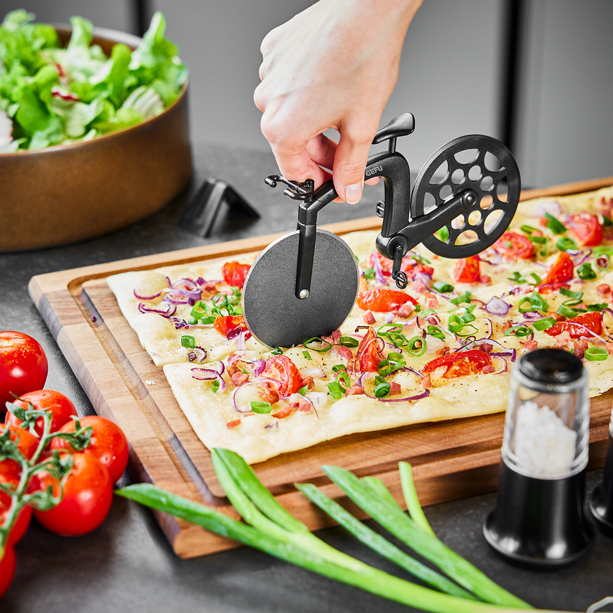 Pizzaschneider in Form eines Fahrrads schneidet Fladenbrot mit Tomaten